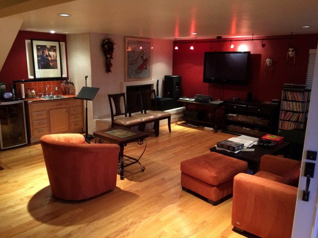 A warm den with wooden floors, orange armchairs, a leather ottoman and artwork on deep red walls